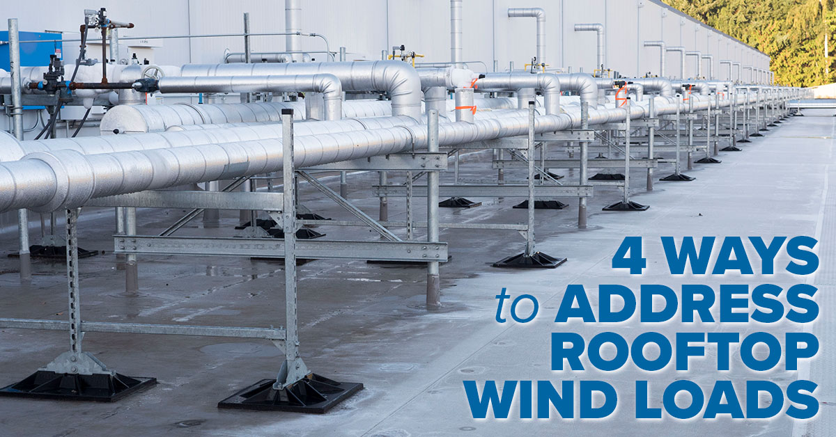 Photo of rooftop pipe supports with wind and seismic compliant bases. The supports are h-frames and they are supporting ammonia pipping on a commercial rooftop